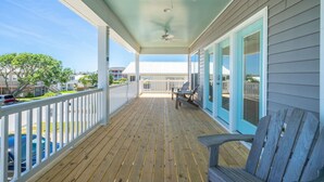 A covered porch with a ceiling fan, wooden deck, and a view of the neighborhood. - 🌊SeaWave: Spacious Pet-Friendly House with Deck & Grill | Walk 2 Beach🌊 (Kure Beach)