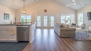 A spacious living area with a kitchen, a dining area, and a large window providing natural light. - 🌊SeaWave: Spacious Pet-Friendly House with Deck & Grill | Walk 2 Beach🌊 (Kure Beach)