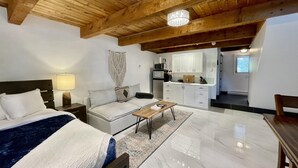 A modern hotel room with a bed, a sofa, a dining table, and a kitchen area. - Waterfront | Hot Tub | Firepit | King Bed - 6H (Ucluelet)