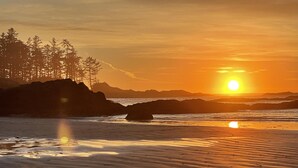 A beach scene with a sunset, rocky formations, and trees. - Waterfront | Hot Tub | Firepit | King Bed - 6H (Ucluelet)