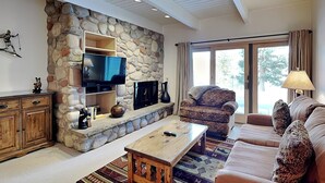 Un salon avec un mur en pierre, un téléviseur à écran plat, un canapé, une table basse et un tapis à motifs.