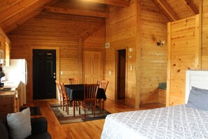 A wooden cabin interior with a dining area, a kitchen, and a bedroom.