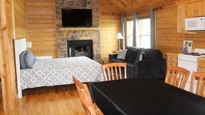 L’intérieur d’une cabane en rondins comprend un lit, un canapé, une table à manger, une cheminée, un téléviseur et un coin cuisine.