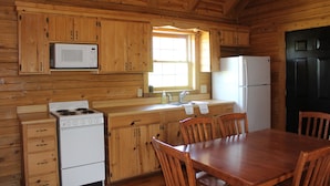 Une cuisine rustique aménagée dans une cabane en bois, avec un poêle, un four à micro-ondes, un réfrigérateur et des placards en bois.