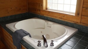 L’intérieur d’un chalet en bois, avec une grande baignoire, une fenêtre et une serviette posée sur le bord.