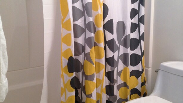 Une salle de bain avec des toilettes blanches, une baignoire et un rideau de douche à motifs géométriques.