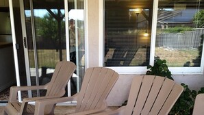 Trois chaises en plastique de couleur beige sont disposées sur une terrasse en béton. On aperçoit, à l’arrière-plan, une porte et une fenêtre en verre.