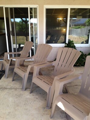 Trois chaises en plastique de couleur beige sont disposées sur une terrasse en béton. On aperçoit, à l’arrière-plan, une porte et une fenêtre en verre.