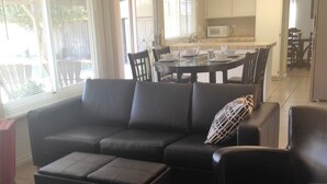 A living room with a sectional sofa, a red ottoman, and a black armchair. There is a dining area with a table and chairs in the background. - Large house in Silicon Valley - 40 min from San Francisco near Levi's Stadium (Santa Clara)