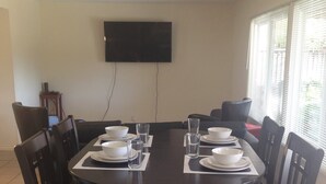 A dining area with a round table set for six, surrounded by dark wooden chairs. A flat-screen TV is mounted on the wall above the table. - Large house in Silicon Valley - 40 min from San Francisco near Levi's Stadium (Santa Clara)