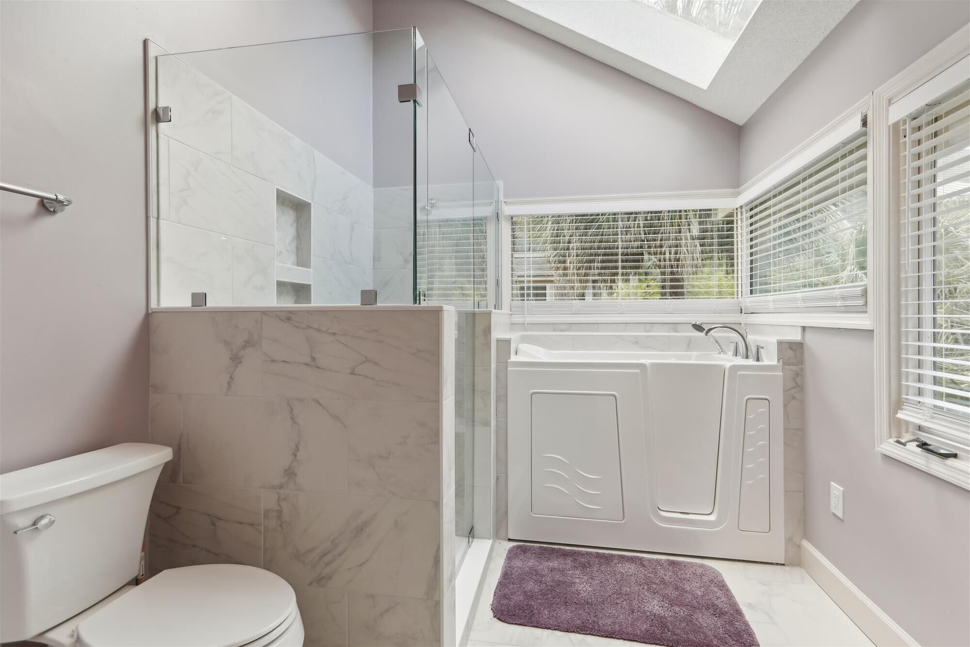 A bathroom with a glass-enclosed shower, a toilet, a bathtub, and a window with blinds.