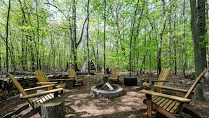 A forest clearing with a fire pit, wooden chairs, and a table. - Newly Updated Union Pier Home with Deeded Beach Access! (Union Pier)