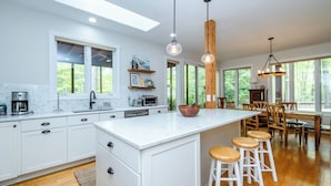 A modern kitchen with white cabinets, a large island, bar stools, and pendant lighting. - Newly Updated Union Pier Home with Deeded Beach Access! (Union Pier)