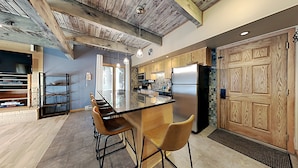 A modern kitchen with a central island, bar stools, wooden cabinets, and a large wooden door. - 🌲Timberline C2E Deluxe 2-Bedroom ~Hot Tub~Pool~WiFi~Ski-in/out~Local Shuttle🌲 (Snowmass Village)