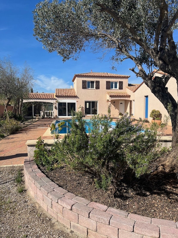 A two-story house with a tiled roof, a swimming pool, and a landscaped garden.