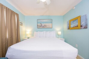 Une chambre d’hôtel avec un lit, deux lampes fixées au mur, un ventilateur de plafond et deux tableaux encadrés accrochés au mur.