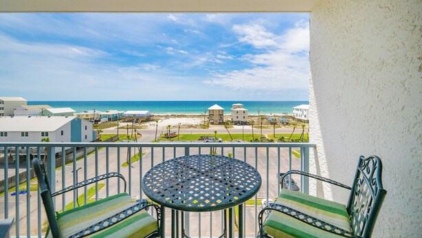 Ein Balkon mit Tisch und Stühlen, mit Blick auf einen Strand und Gebäude.