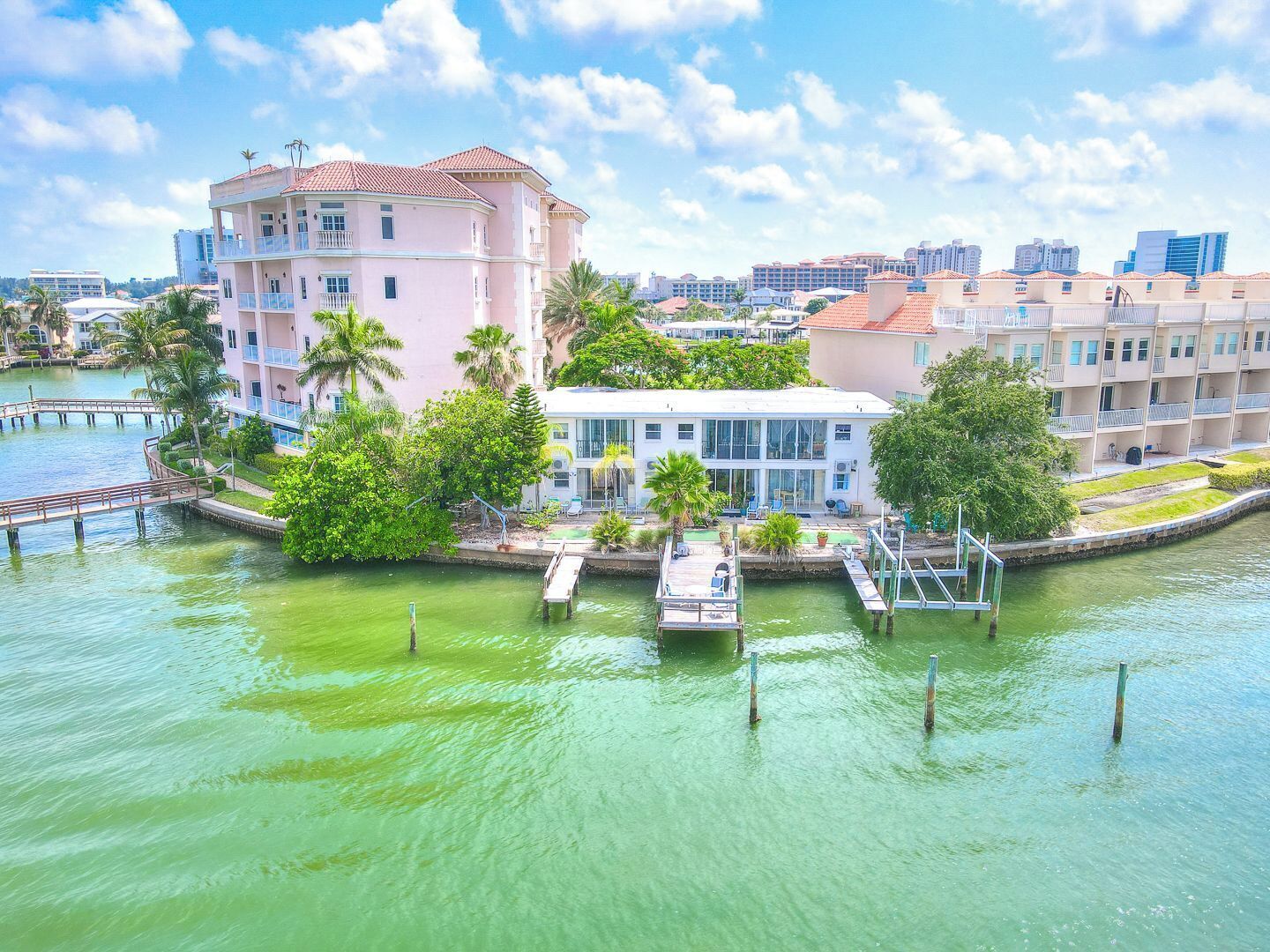 A waterfront hotel with a dock, palm trees, and a cityscape in the background.