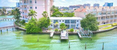 A waterfront hotel with a dock, palm trees, and a cityscape in the background.