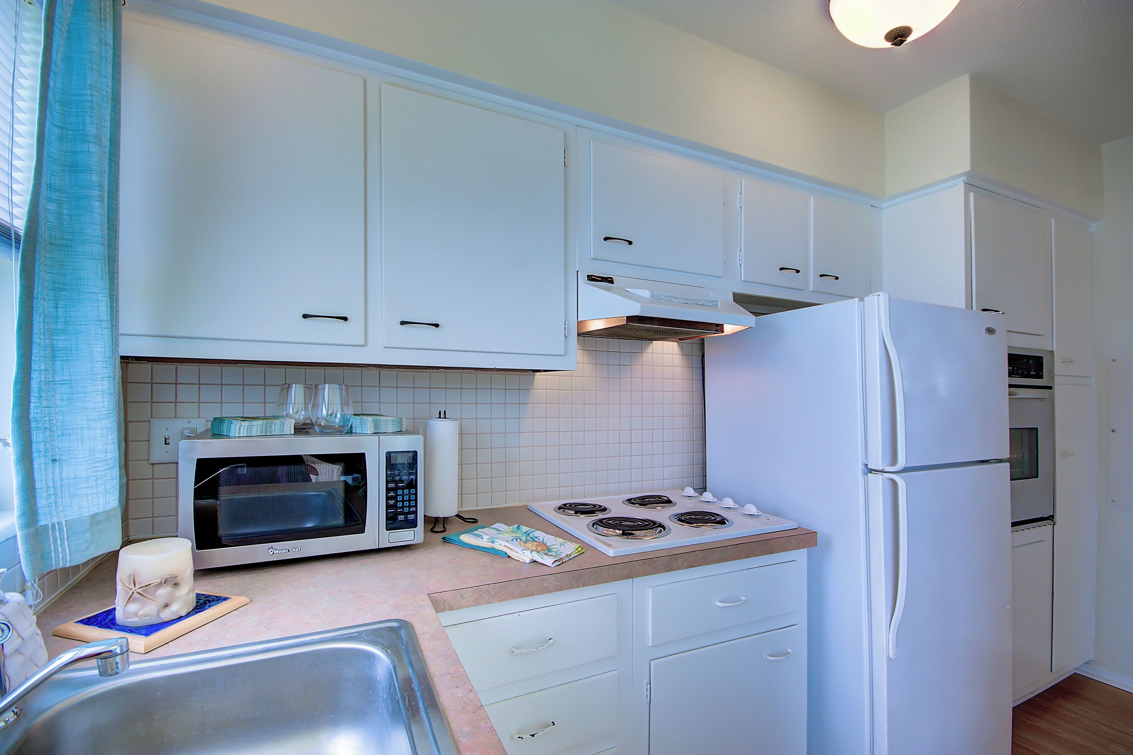 Una cocina con armarios blancos, microondas, estufa y refrigerador.