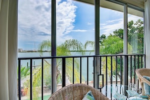A balcony with a view of a lake, wicker furniture, and a glass table.