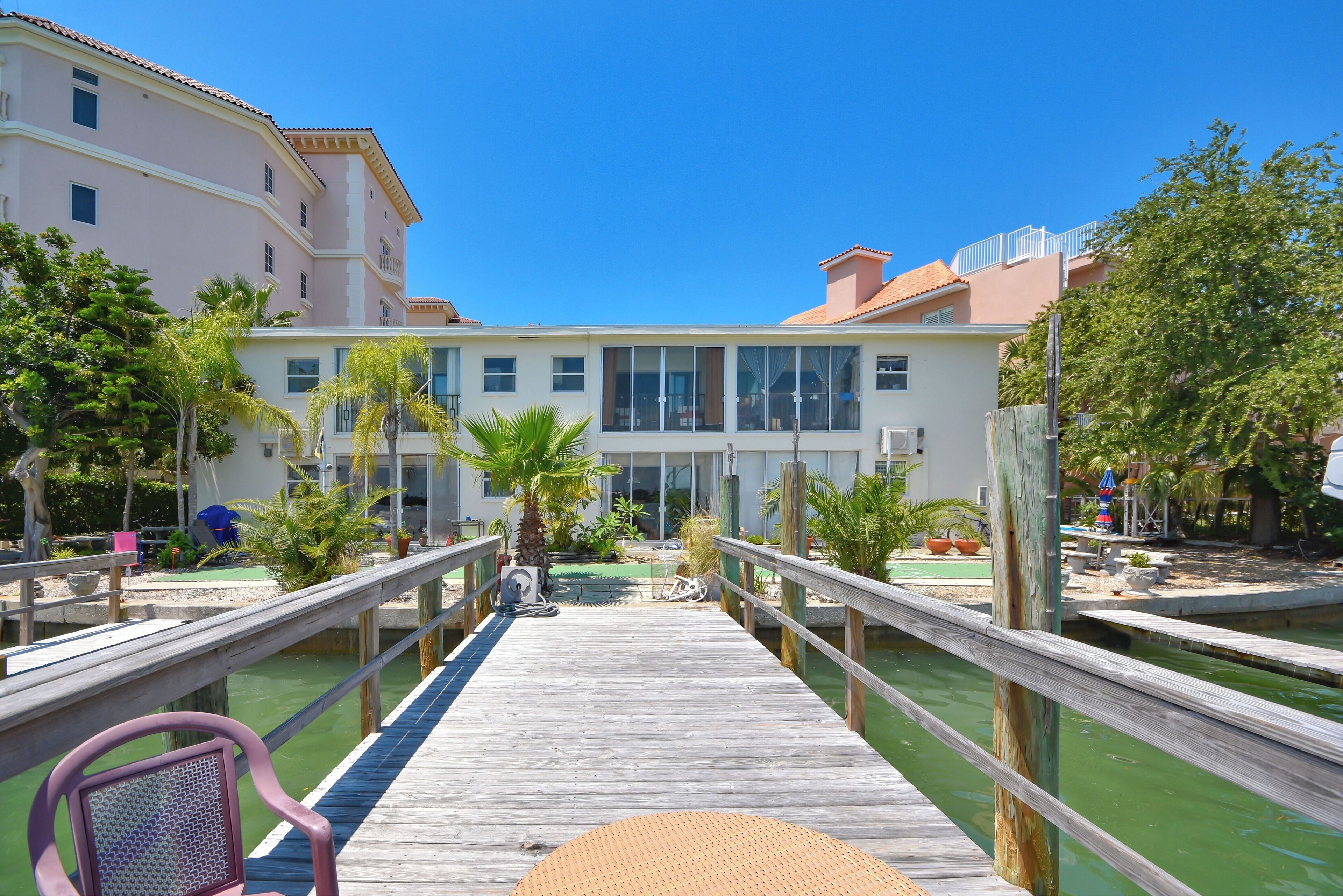 A wooden pier leading to a building with large windows and a pool area.