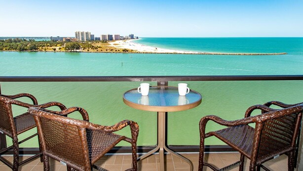 Ein Balkon mit Korbstühlen und einem Tisch, mit Blick auf Strand und Stadtlandschaft.