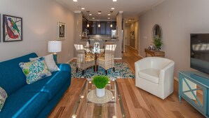Un salon moderne avec un canapé bleu, un fauteuil blanc et une table basse en verre sur laquelle est posée une plante verte.