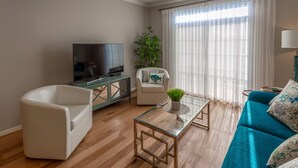 Un salon équipé d’un téléviseur à écran plat, d’un fauteuil blanc, d’un canapé turquoise, d’une table basse en verre et d’un ventilateur de plafond.