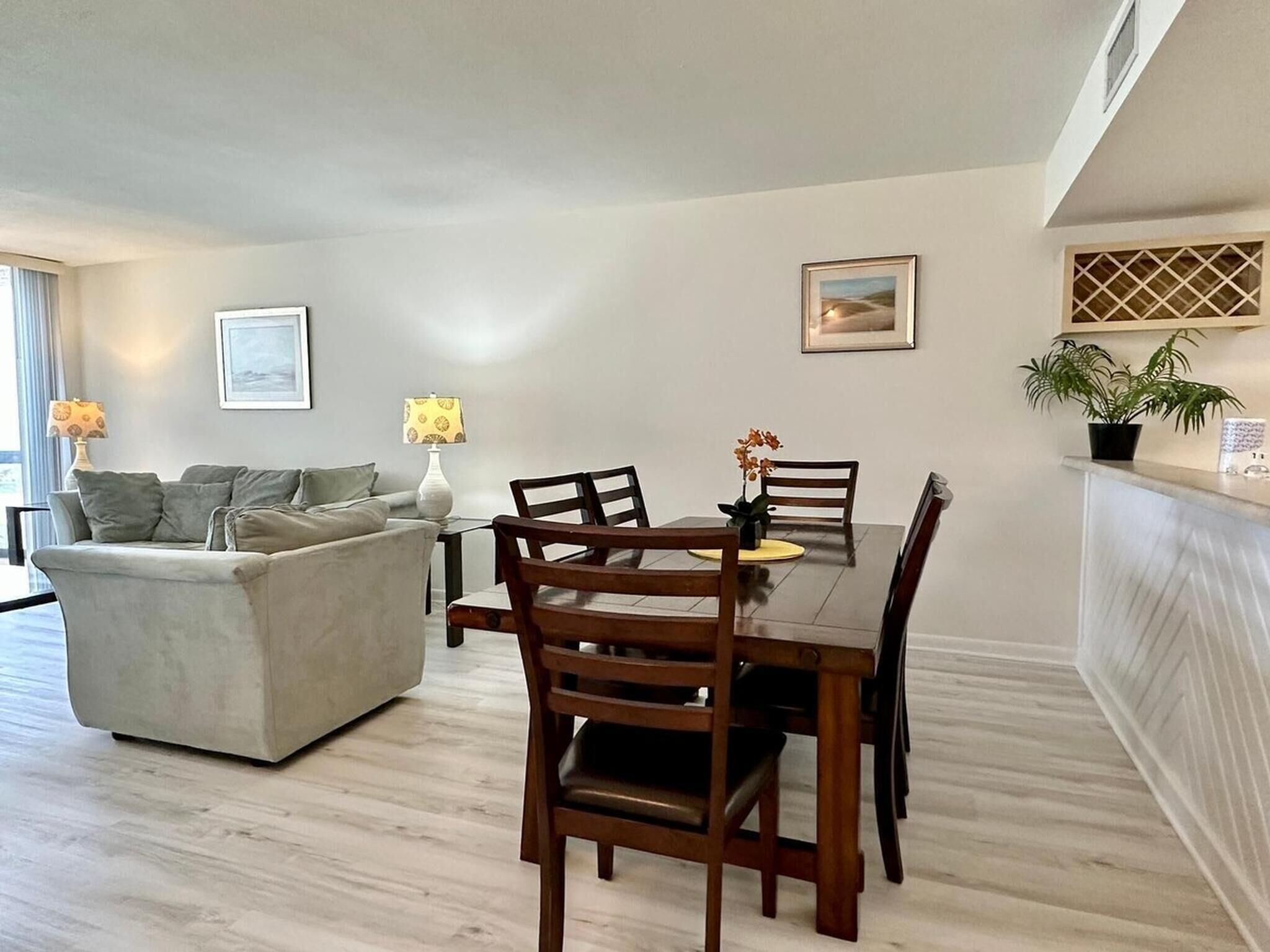 A modern living room with a dining area, a sofa, a table with chairs, a lamp, and a potted plant.