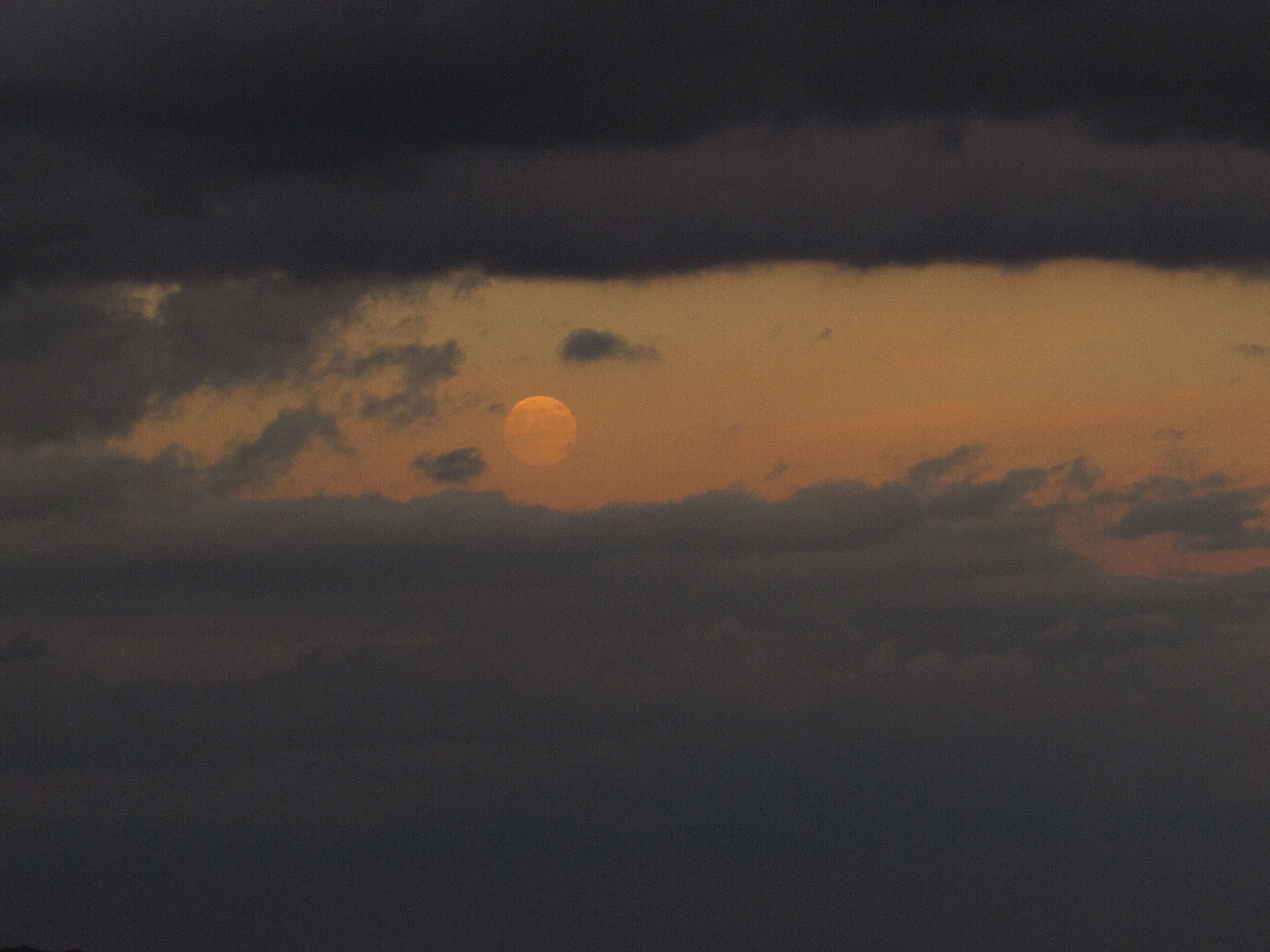 A full moon partially obscured by clouds against a dusky sky.