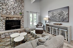 A living room with a stone fireplace, a large painting, and a bar area. - 🌲Timberline D3E Deluxe 3-Bedroom plus Loft ~Hot Tub~Pool~WiFi~Ski-in/out~Local Shuttle🌲 (Snowmass Village)