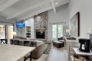 A modern living room with a stone fireplace, a flat-screen TV, and a dining area with a coffee machine. - 🌲Timberline D3E Deluxe 3-Bedroom plus Loft ~Hot Tub~Pool~WiFi~Ski-in/out~Local Shuttle🌲 (Snowmass Village)