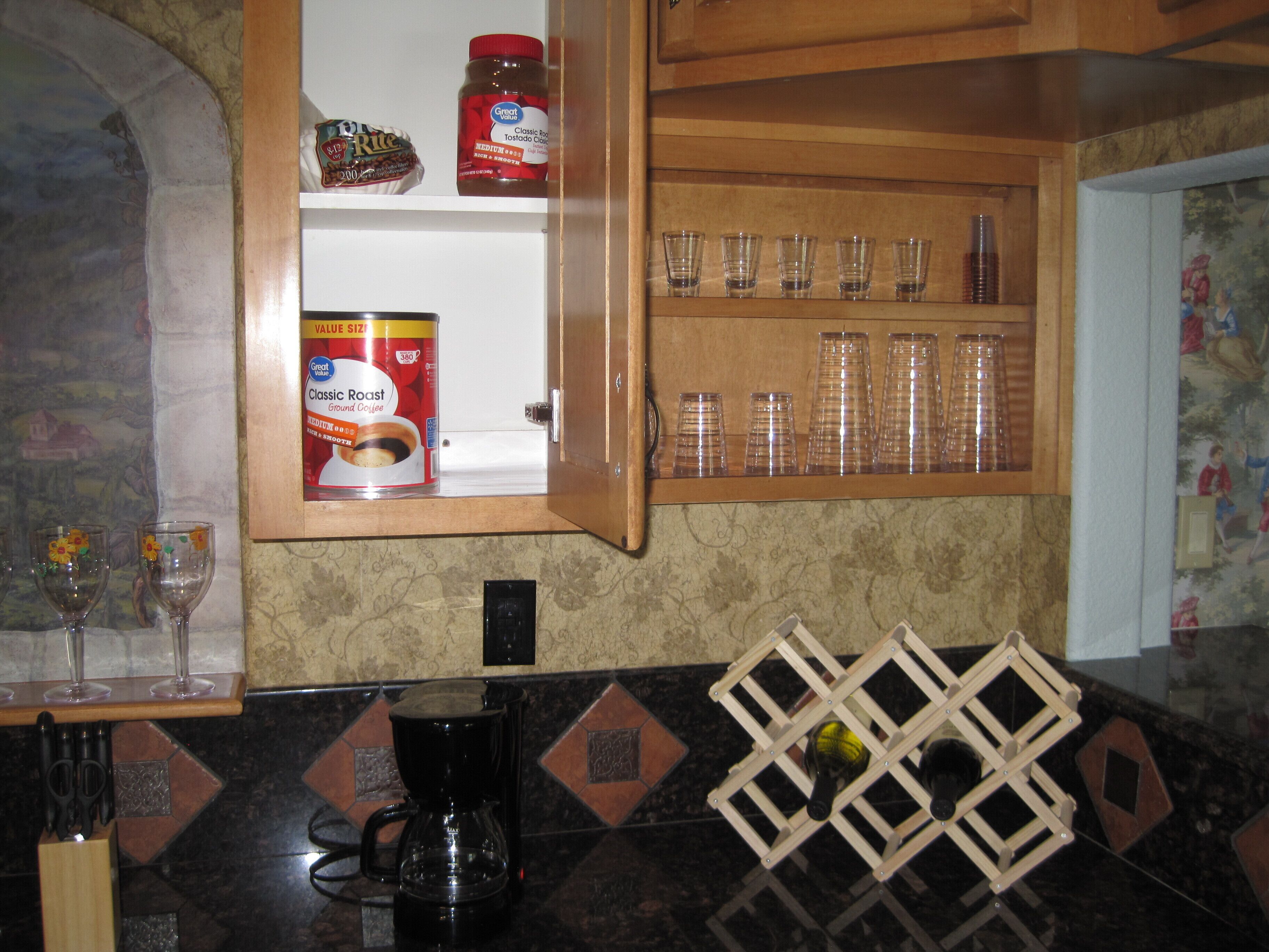 A kitchen with a coffee maker, a spice rack, and a cabinet with glassware.