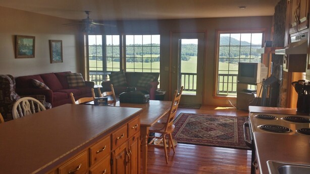 A spacious kitchen with a large island, wooden cabinets, and a view of a green landscape through the windows. - Calico Rock Cabin-500 Calico St 390 Chessmond Ferry Rd viewing the White River  (Calico Rock)