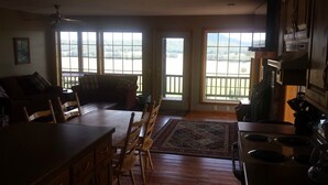 A spacious kitchen with a large island, wooden chairs, and a dining table. There are large windows offering views of a forested area. - Calico Rock Cabin-500 Calico St 390 Chessmond Ferry Rd viewing the White River  (Calico Rock)
