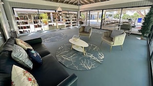 A spacious indoor area with a high ceiling, a ceiling fan, and a large open space with a sofa, chairs, and a coffee table. There are bookshelves and a view of the outdoors through large windows. - 2 Bdrm Monthly ocean view, expansive porch ,renovated unit Key West Fabulous (Key West)