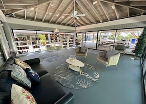 A spacious indoor area with a ceiling fan, a sofa, two armchairs, a coffee table, and a bookshelf filled with books.