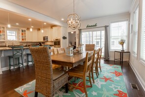 Uma cozinha ampla com armários brancos, uma mesa de jantar de madeira com cadeiras e um tapete decorativo com estampas de estrelas-do-mar.
