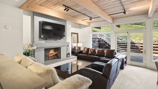 A modern living room with a fireplace, leather sofas, a flat-screen TV, and a wooden ceiling.