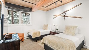A bedroom with two beds, a desk, a chair, and a window with a view of trees.