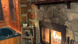 A cozy room with a stone fireplace, a wooden bathtub, and a framed picture on the wall.