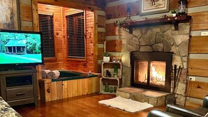 A cozy living room with a fireplace, wooden walls, a pool table, and a leather sofa.