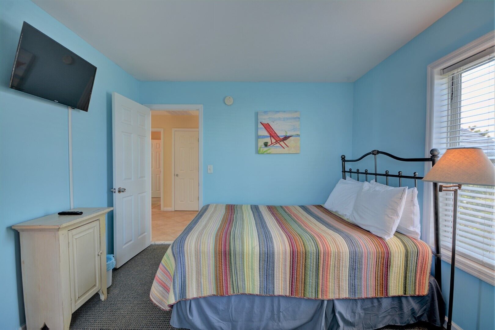 A bedroom with a bed, a TV, a painting, and a lamp.