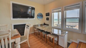 A kitchen with a TV, a fireplace, a bar area, and a view of the beach. - Five Bedroom Oceanfront Home - Just Chilln (North Topsail Beach)