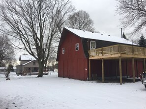 Una cascina rossa con una veranda in legno, circondata da terreno innevato e alberi spogli.