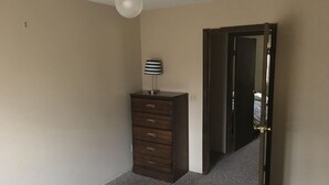 Quarto com cama, penteadeira, ventoinha no teto e porta para outro espaço.