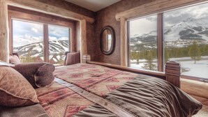 A cozy room with a large bed, a chair, and a view of snow-capped mountains through large windows.