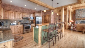 A rustic kitchen with wooden cabinets, a central island with bar stools, a stove, and a refrigerator.