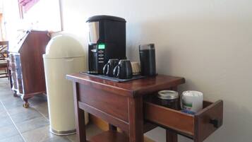 A coffee station with a coffee maker, mugs, and a thermos on a wooden table.